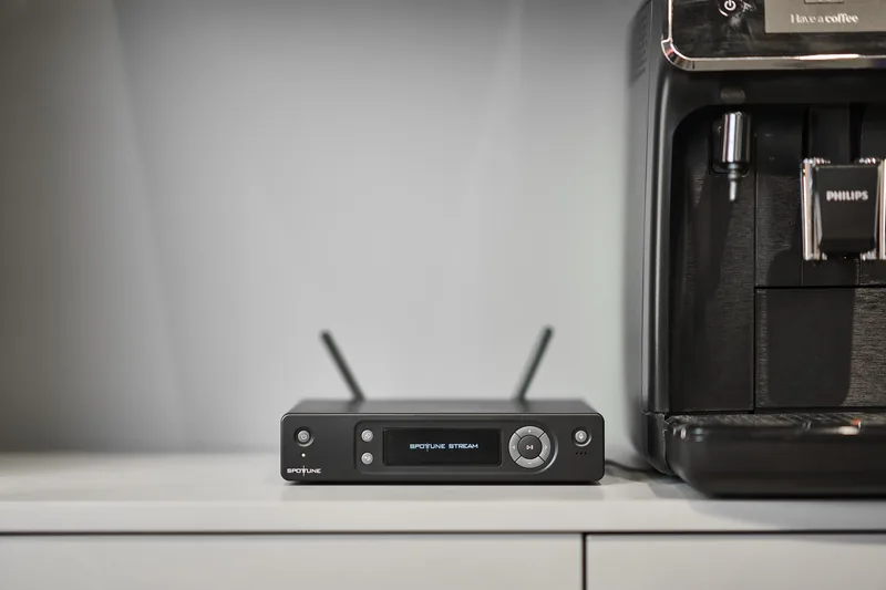 Stream negro con sus dos antenas sobre un mostrador blanco, junto a una máquina de café.