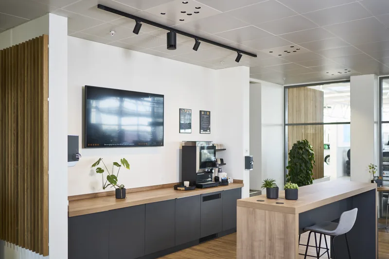 Zona de café de una oficina con cocina negra, pantalla en la pared y Omni Track negros en un riel negro.