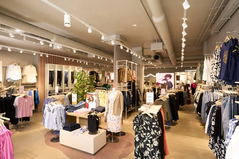 Vista amplia de una tienda de moda con varios Omni Track blancos en los rieles del techo y mesas de exhibición.