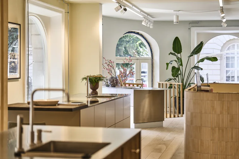 Sala de exhibición de cocinas con ventanas en arco, isla de madera y Omni Track blancos en el riel.